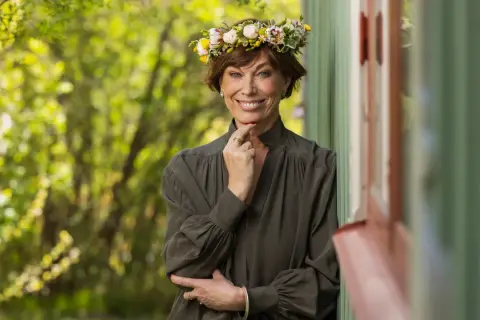 En kvinna med blomsterkrans ler mot kameran. Hon påminner om en sommarbild av mischa billing familj.