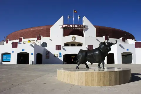 Escultura de toro frente a la Plaza de Toros Roquetas de Mar, bajo un cielo azul intenso.