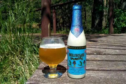 Piwo Delirium Tremens w szklance i butelce, na drewnianym tarasie wśród zieleni.