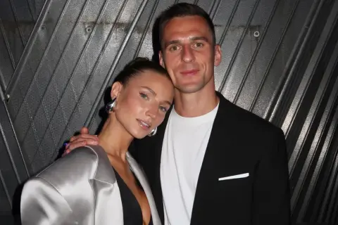 Agata Sieramska i jej partner pozują do zdjęcia. Ona ma na sobie srebrną marynarkę i dużą, metaliczną biżuterię.