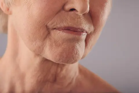 Primo piano del volto di un'anziana, con labbra sottili e rughe della marionetta che raccontano storie di vita.