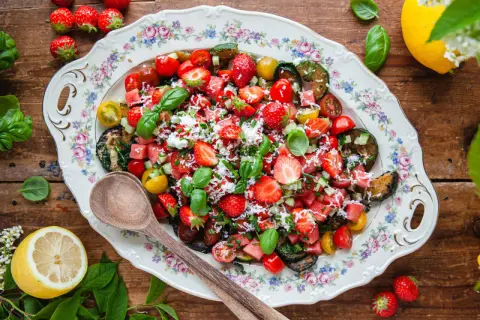 En härlig somrig sallad med jordgubbar, vattenmelon, tomater och basilika på ett vackert fat.