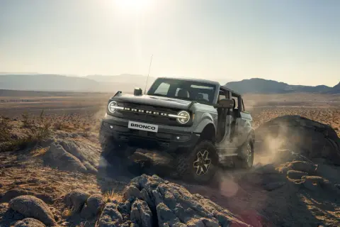 Ford Bronco pokonuje skalisty teren pustyni, wzbijając tumany kurzu.