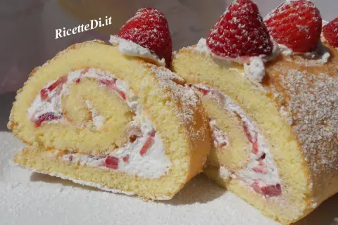 Un delizioso rotolo panna e fragole, soffice pan di Spagna arrotolato con crema e pezzetti di fragole fresche, decorato con zucchero a velo e fragole intere.