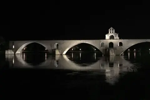 Nocna panorama na moście w Avignon. Kamienne łuki odbijają się w spokojnej wodzie rzeki Rodan.