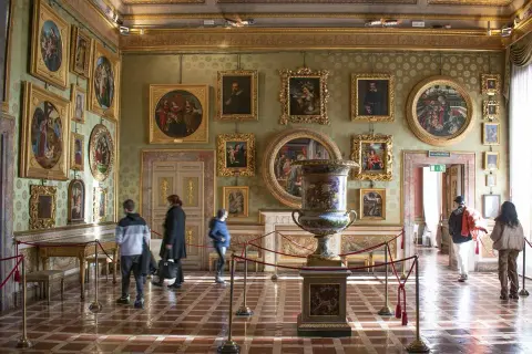 Interno di una sala del Palazzo Pitti, con opere d'arte alle pareti, un grande vaso e visitatori.