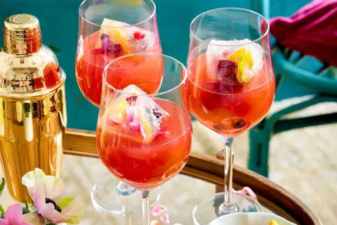 Erfrischendes Aperol Spritz Rezept: Drei Gläser mit leuchtend rotem Aperol, Eiswürfeln und Fruchtgarnitur. Ein goldener Shaker steht bereit.