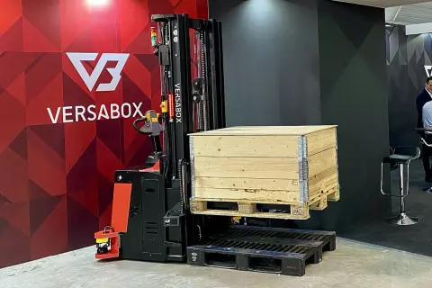 AGV robot VersaBox podnosi drewnianą skrzynię na palecie.