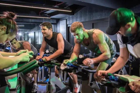 Intensywny trening spinningowy. Grupa ludzi pedałuje na rowerach stacjonarnych, skupiona na wysiłku.