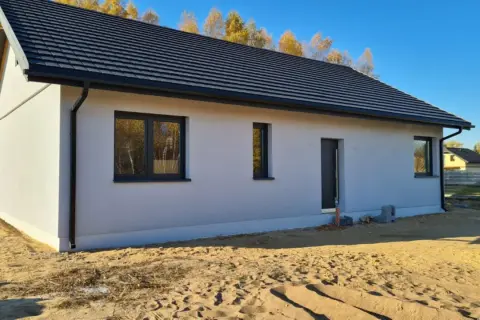Nowy dom z szarym dachem i białymi ścianami, z oknami i drzwiami, w stanie surowym zamkniętym.