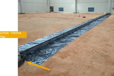 Instalación de una solera de hormigón con armadura metálica sobre plástico negro en interior de nave.