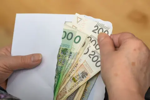 Dłonie wyciągają z koperty polskie banknoty. To może być pomoc finansowa, emerytura po mężu, czy oszczędności.