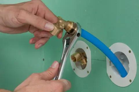 Installation d'un raccord pour l'arrivée d'eau de la douche. Une clé serre un coude en laiton sur un tuyau bleu.