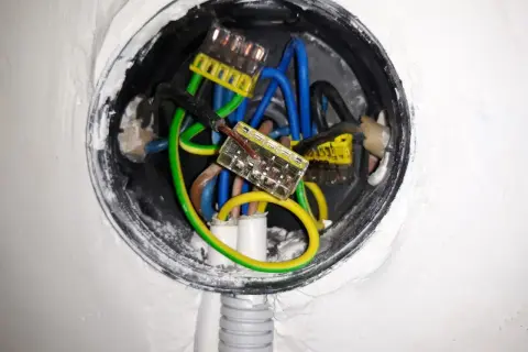 W puszce elektrycznej widać połączenia przewodów: niebieskich, zielono-żółtych i czarnych. Wygląda na to, że trwa zerowanie instalacji.