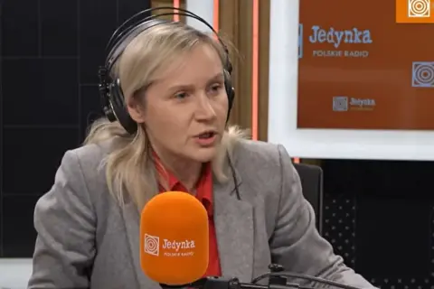 Kobieta w słuchawkach, przypominająca żonę Michała Rachonia, udziela wywiadu w studiu Polskiego Radia Jedynka.