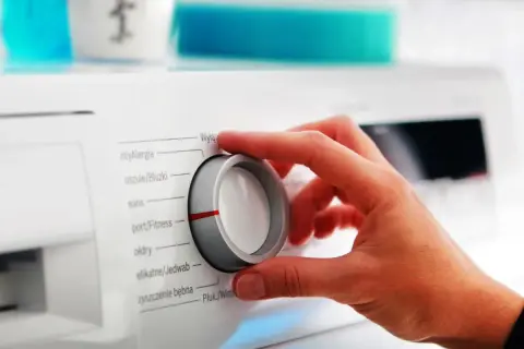 Dłoń kręci pokrętłem pralki, wybierając program. Szukamy cichej pralki, ile decybeli?