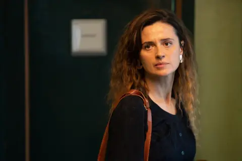 Agnieszka Grochowska, z brązową torbą na ramieniu, patrzy w bok zamyślona.