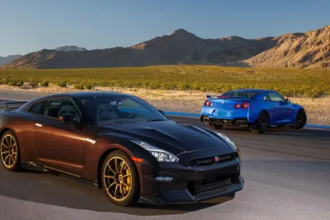 Dwa Nissan GTR R35, jeden brązowy, drugi niebieski, stoją na torze wyścigowym na tle pustynnego krajobrazu.