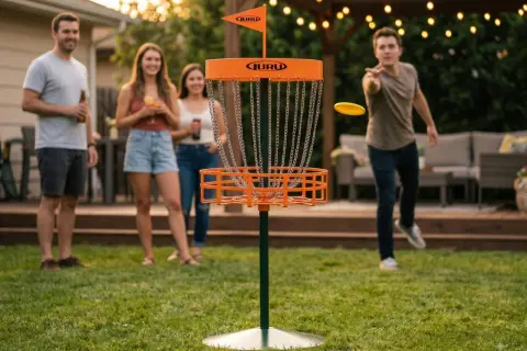 Vänner njuter av en inflyttningsfest med discgolf-lekar i trädgården. En man kastar en gul disc mot korgen.