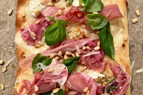 En läcker pinsa bianco med tunt skivad prosciutto, pinjenötter, färsk basilika och krämig ost.