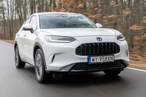 Biały Honda ZR-V jedzie po drodze wśród drzew.