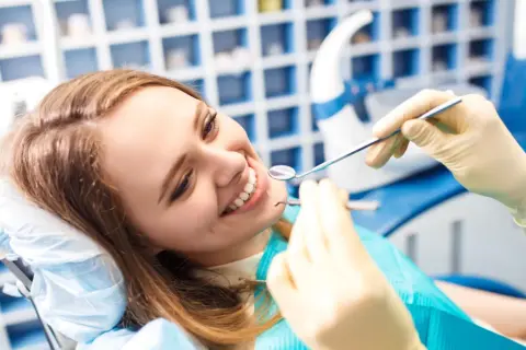 Uśmiechnięta kobieta u dentysty, badanie zębów lusterkiem i narzędziem.