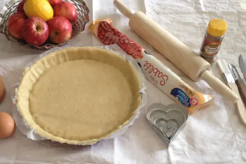 Préparation d'une tarte aux pommes simple : pâte sablée, pommes, citron, œuf, rouleau, emporte-pièces cœur et cannelle.