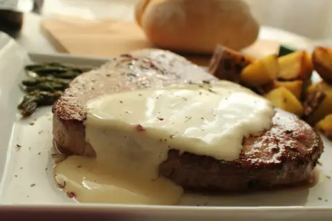 Filete redondo cubierto con una cremosa salsa blanca, acompañado de espárragos y patatas asadas.