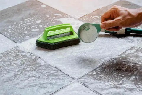 Une main verse une poudre nettoyante sur un carrelage très encrassé, prêt à être brossé.