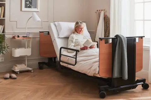 Une femme lit dans un lit médicalisé. Ce type de table de lit médicalisé est souvent éligible au remboursement de la Sécurité Sociale.