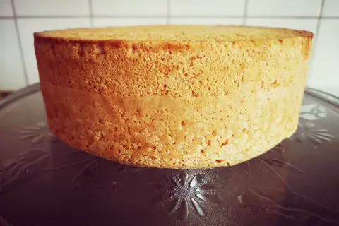 En gyllene anslag tårta med en porös textur står på ett mönstrat fat. Den är redo att dekoreras för ett speciellt tillfälle.
