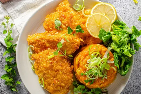 Knuspriges Zucchin Schnitzel mit Kürbispüree, Salat und Zitronenspalten.