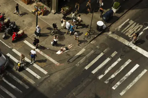 Un homme sur une planche de surf traverse une rue animée, une scène capturée par Romain Laurent.