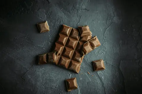 Tableta de chocolate rota y trozos sueltos sobre fondo oscuro. ¡Sí, puedo llevar chocolates en la maleta de mano!