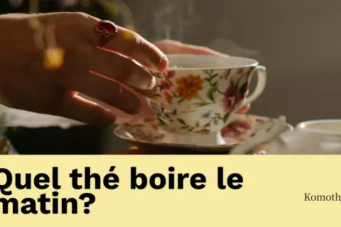 Une main ornée d'une bague saisit une tasse de thé fumante, ornée de fleurs. La question "Quel thé boire le matin?" invite à découvrir le plaisir d'une boisson matinale.