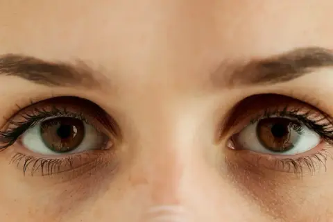 Zbliżenie na oczy z widocznymi cieniami i delikatnymi wory pod oczami, sugerującymi zmęczenie lub brak snu.