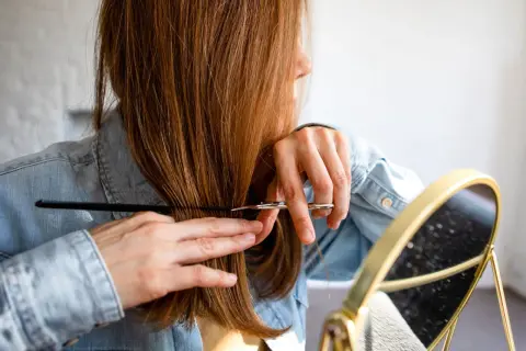 Frau schneidet sich mit Schere und Kamm die Haare, wie in einer stufenschnitt anleitung bilder.