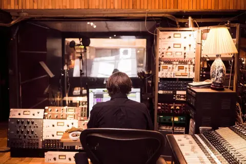 Producent muzyczny w studio, otoczony sprzętem, tworzy nową muzykę, być może z pomocą sztucznej inteligencji.