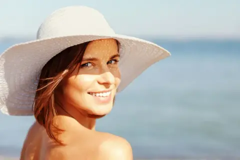 Frau mit Hut am Strand, genießt die Sonne mit Sonnencreme LSF 50 Gesicht.