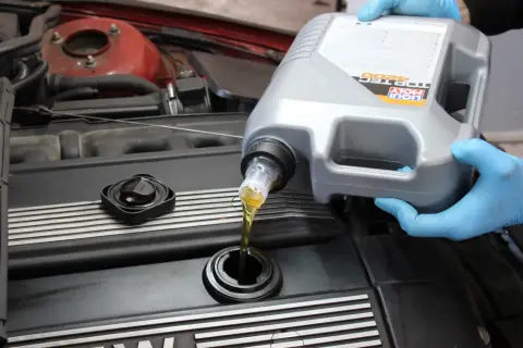 Ręce w niebieskich rękawiczkach wlewają olej silnikowy Liqui Moly do silnika. Czy można mieszać oleje silnikowe? To pytanie nurtuje wielu kierowców.