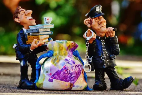Figurki: uradowany mężczyzna z książkami i kubkiem "I LOVE TAX" obok policjanta z kajdankami i torbą pieniędzy. To poświadczenie nieprawdy przykłady.