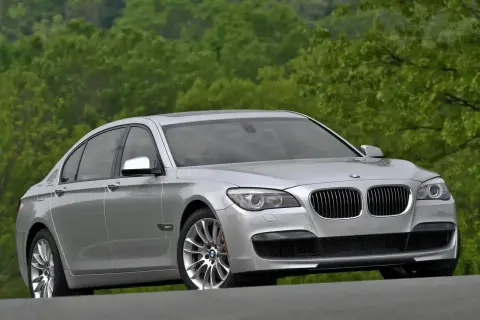 Srebrne BMW 7 F01 na tle zielonych drzew. Elegancka limuzyna prezentuje się okazale na drodze.