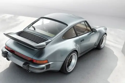 En ikonisk Porsche 80-tals coupé i ljusblått, med sin karaktäristiska bakvinge och breda fälgar.