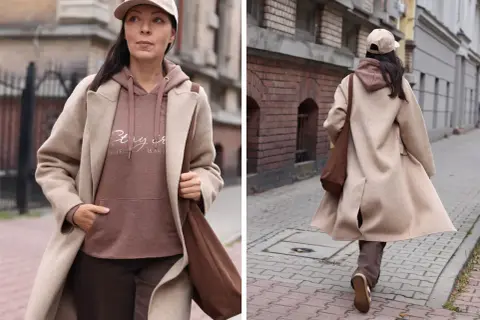 Kobieta w płaszczu w kolorze mlecznej kawy, z bluzą i czapką w podobnym odcieniu, spaceruje ulicą.
