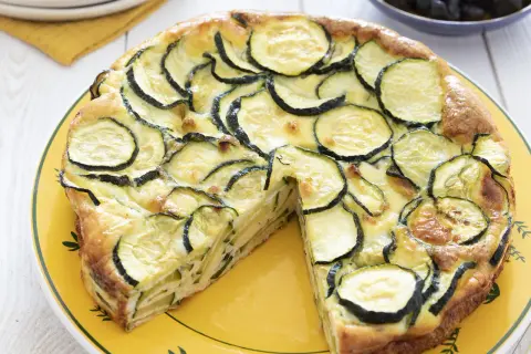 Une délicieuse frittata courgette, garnie de rondelles de courgettes fraîches et dorées, servie sur une assiette jaune.