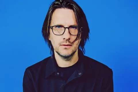Steven Wilson, lider zespołu Porcupine Tree, w okularach i czarnej koszuli na niebieskim tle.