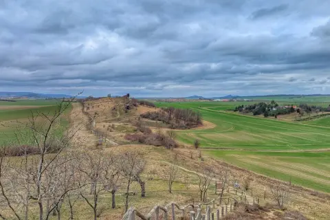 Blick ins Bodetal: Wanderweg führt durch hügelige Landschaft mit grünen Feldern und kahlen Bäumen unter dramatischem Himmel.