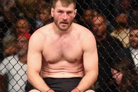 Stipe Miocic, med blodiga sår i ansiktet, sitter utmattad i buren efter en tuff match.