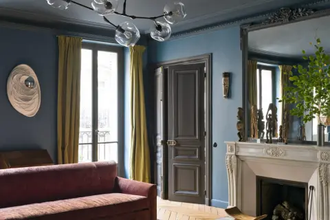 Soggiorno elegante con pareti blu balena Pantone, divano bordeaux, tendaggi ocra e camino in marmo.