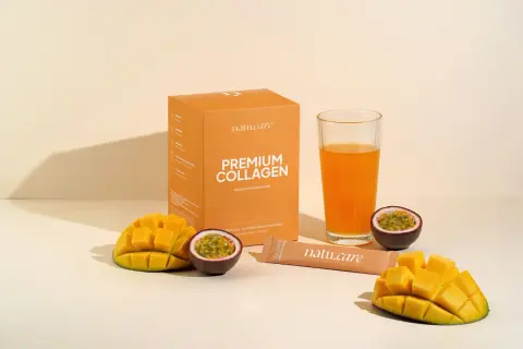 Pudełko z napisem "PREMIUM COLLAGEN Naturalny kolagen rybi", szklanka z pomarańczowym napojem, kawałki mango i marakui.